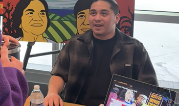 person presents at table with digital humanities project on screen and artwork of dolores huerta over shoulder